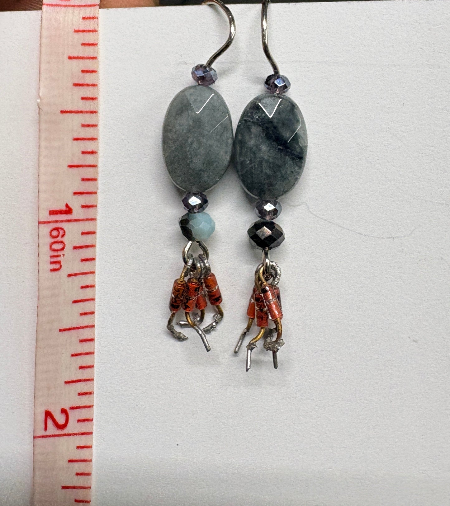Pair of beaded earrings on a white card with a measuring tape for scale.