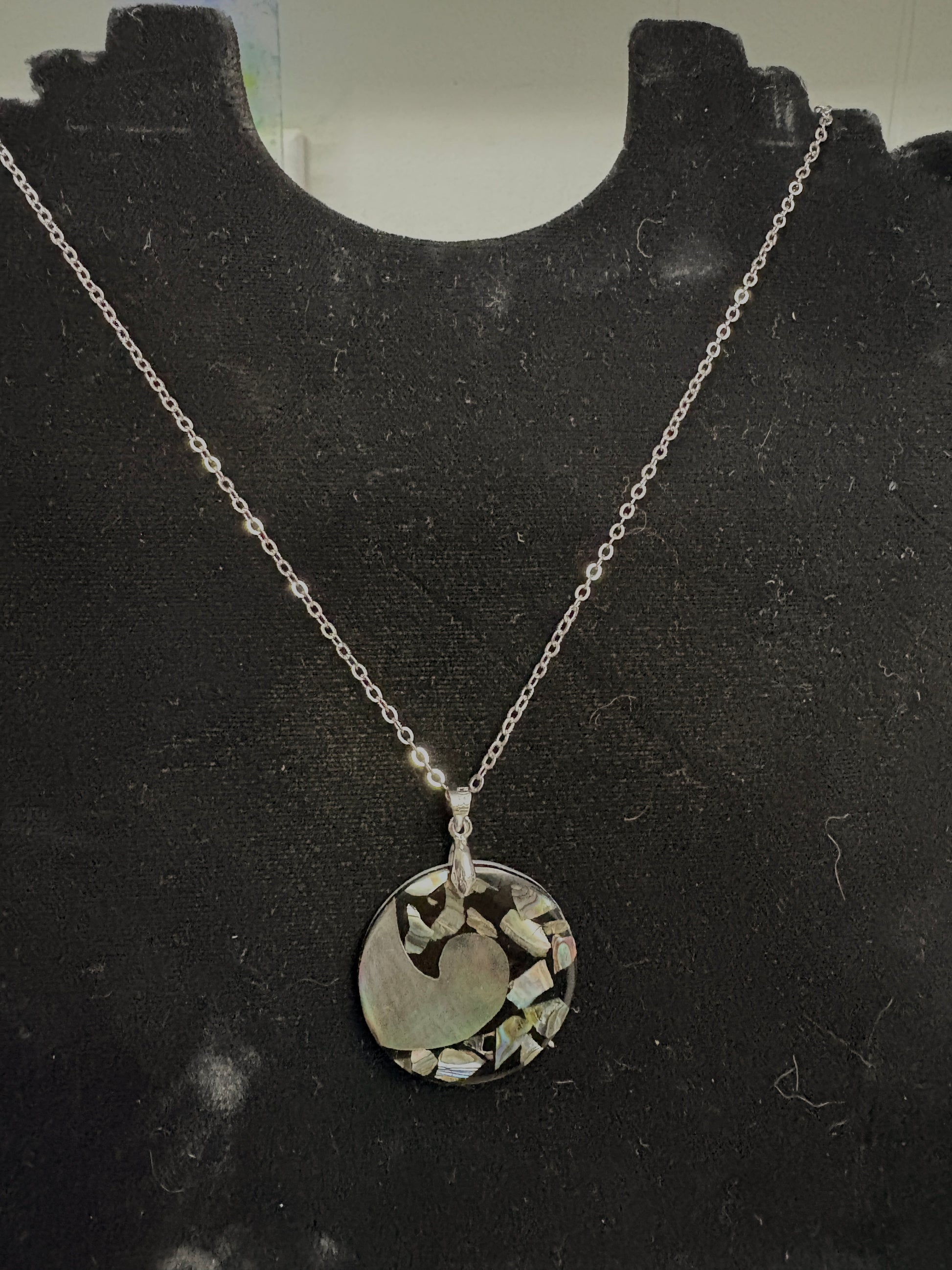 Silver necklace with a circular pendant on a black mannequin bust.