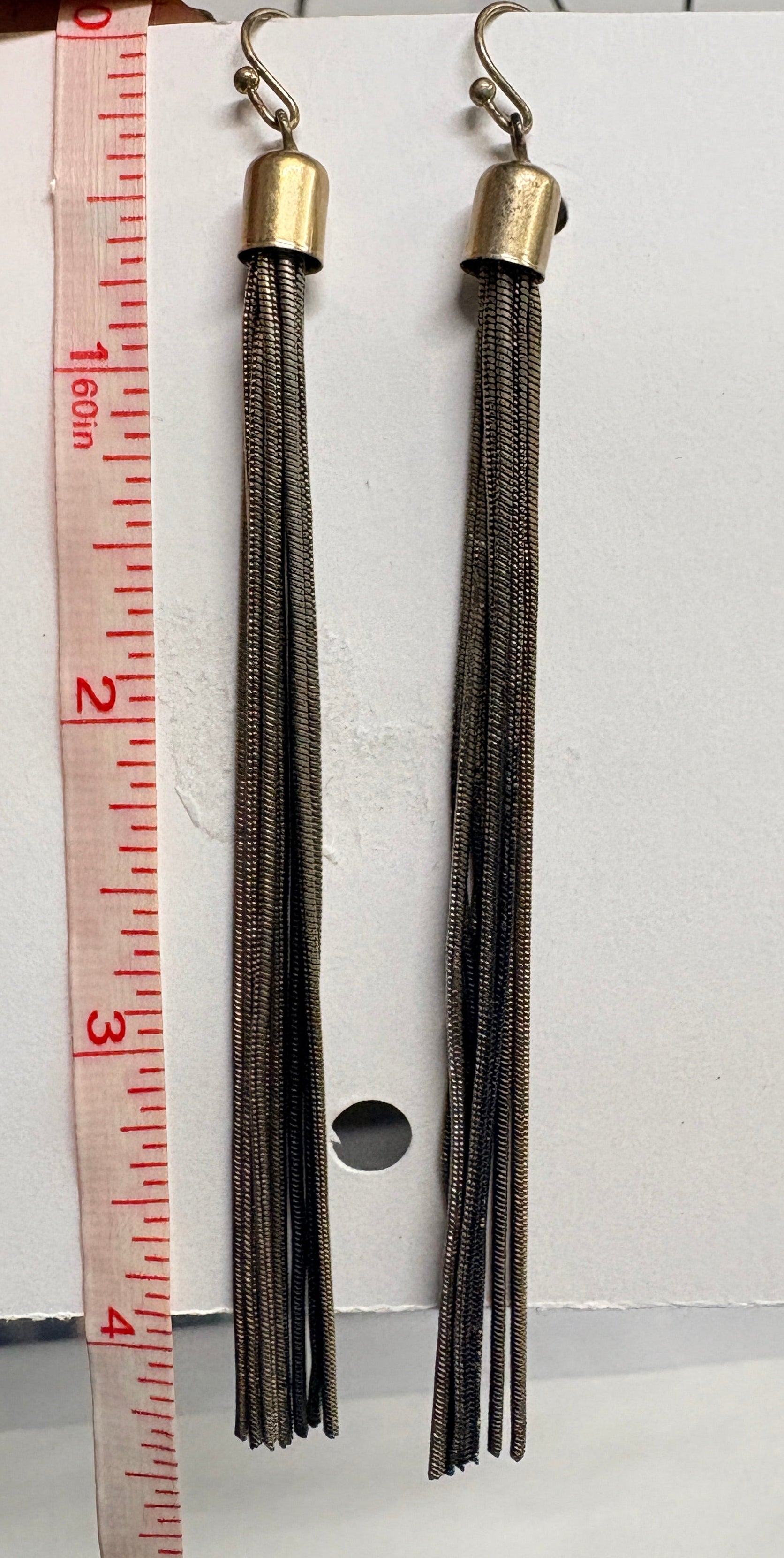 Two tassel earrings on a white card with a ruler for scale