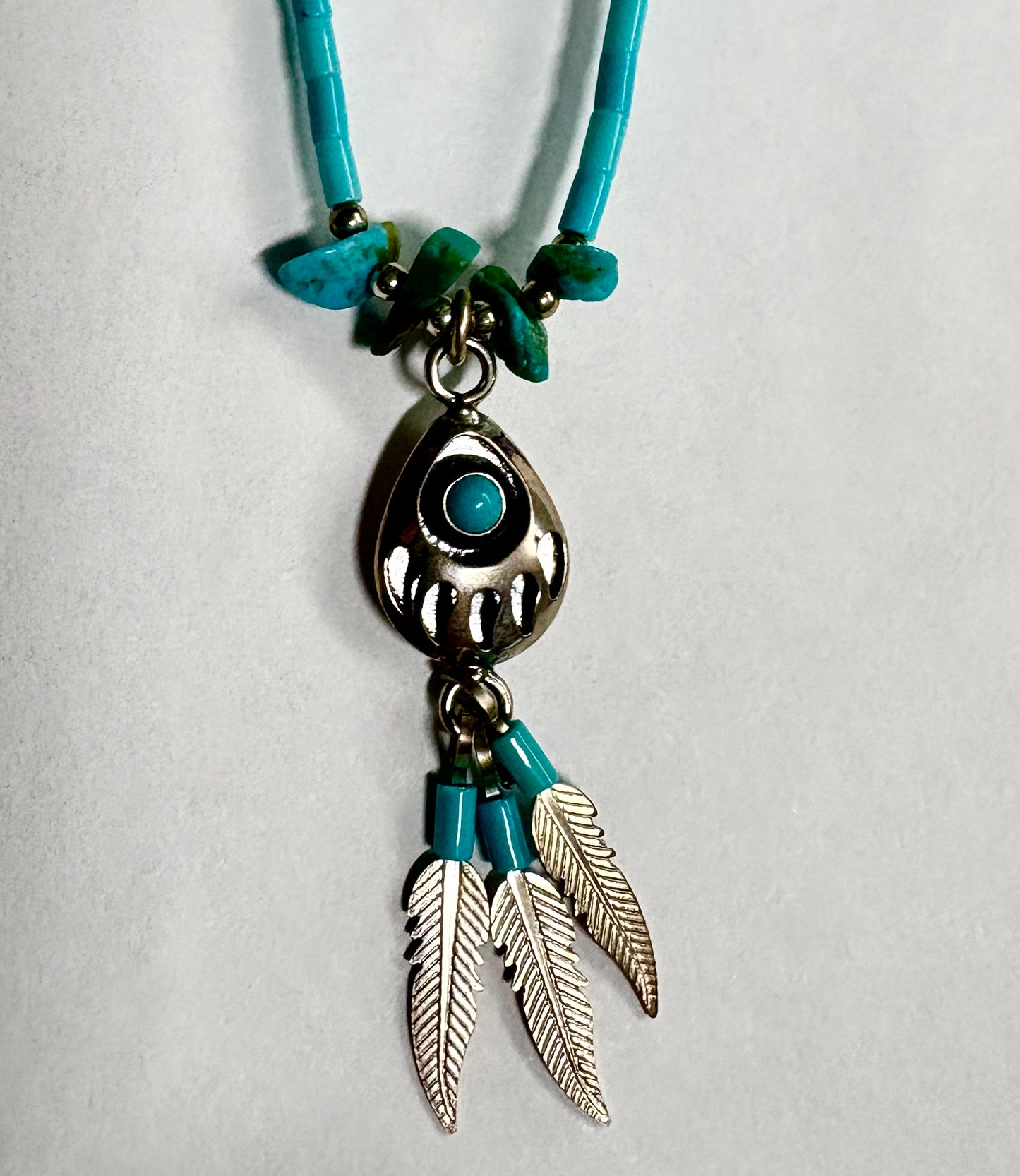 Necklace with turquoise beads and silver feather pendants on a light gray background
