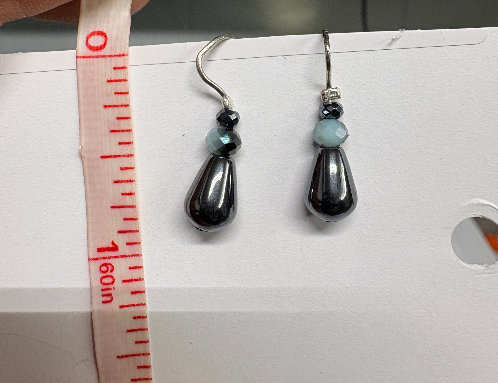 Jewelry earrings being measured with a tape measure against a white background