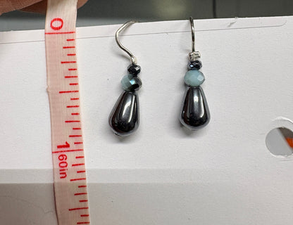 Jewelry earrings being measured with a tape measure against a white background