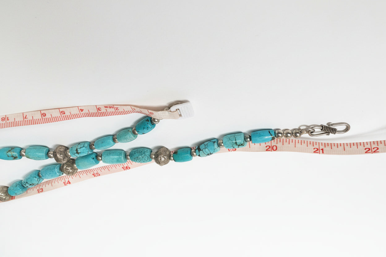 Turquoise beaded lanyard with metal clasps on a white surface with a measuring tape.