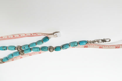 Turquoise beaded lanyard with metal clasps on a white surface with a measuring tape.