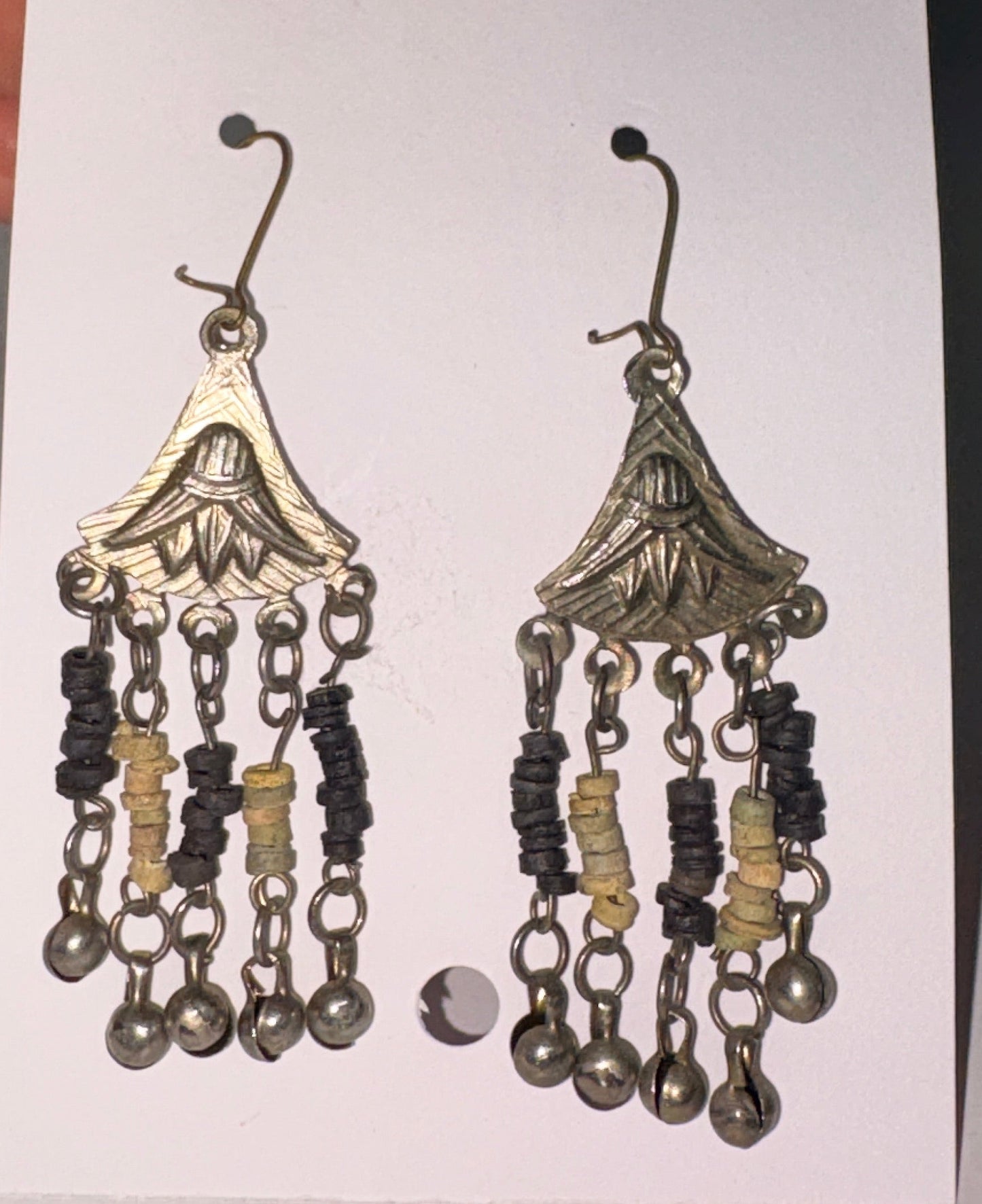 Pair of decorative earrings on a white card held by a hand against a neutral background