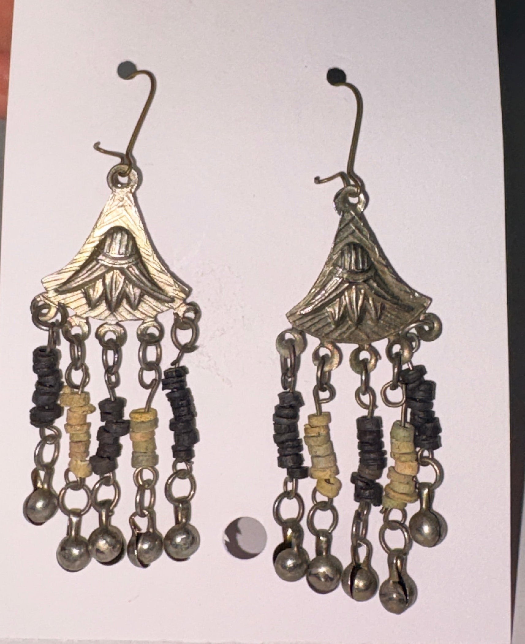 Pair of decorative earrings on a white card held by a hand against a neutral background