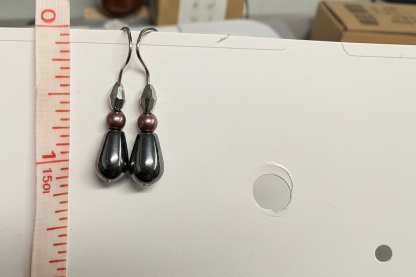 Pair of earrings being measured with a ruler against a sewing machine.