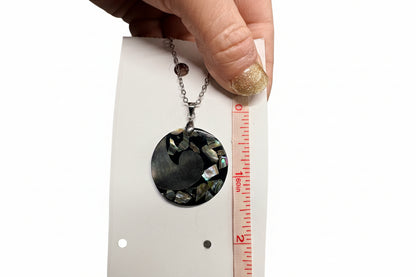 Necklace with a circular pendant being measured against a ruler