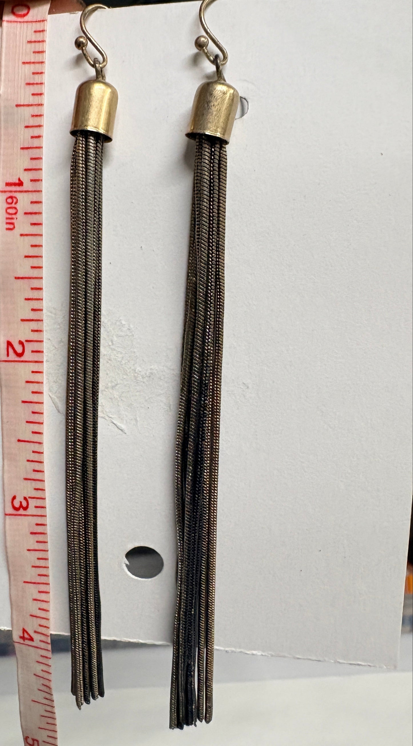 Two pairs of earrings on a white card with a measuring tape for scale.
