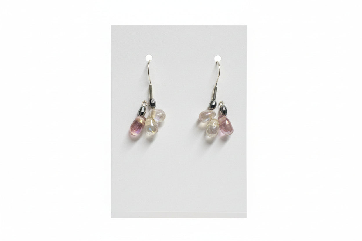 Pair of earrings with gemstones on a white card, held by a hand.