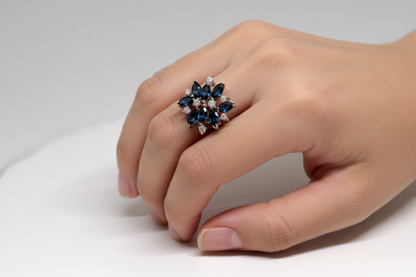 Hand wearing a decorative ring with blue gemstones on a neutral background