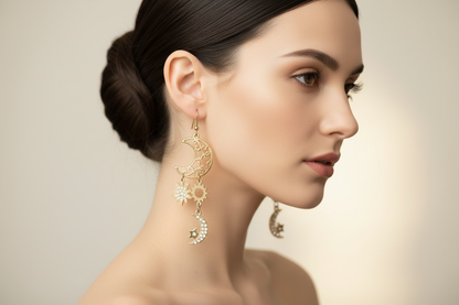 A pair of golden dangle earrings with moon and star designs, adorned with small clear stones.